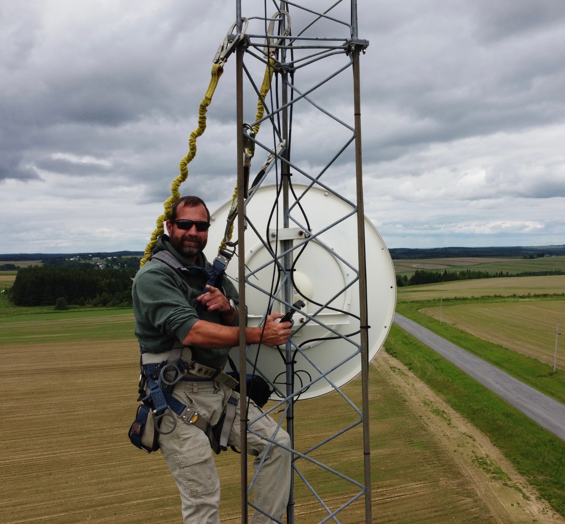 Aroostook Technologies technician working on a microwave dish atop a tower overlooking Aroostook County farmland